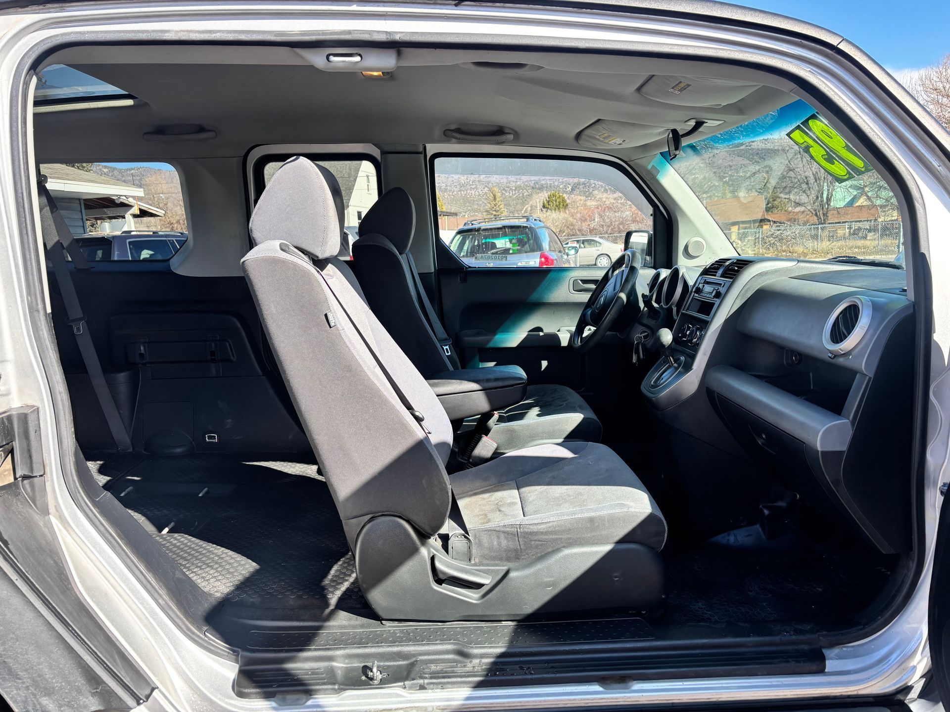 Car interior with rear door open, showing folded seats and dashboard in daylight.