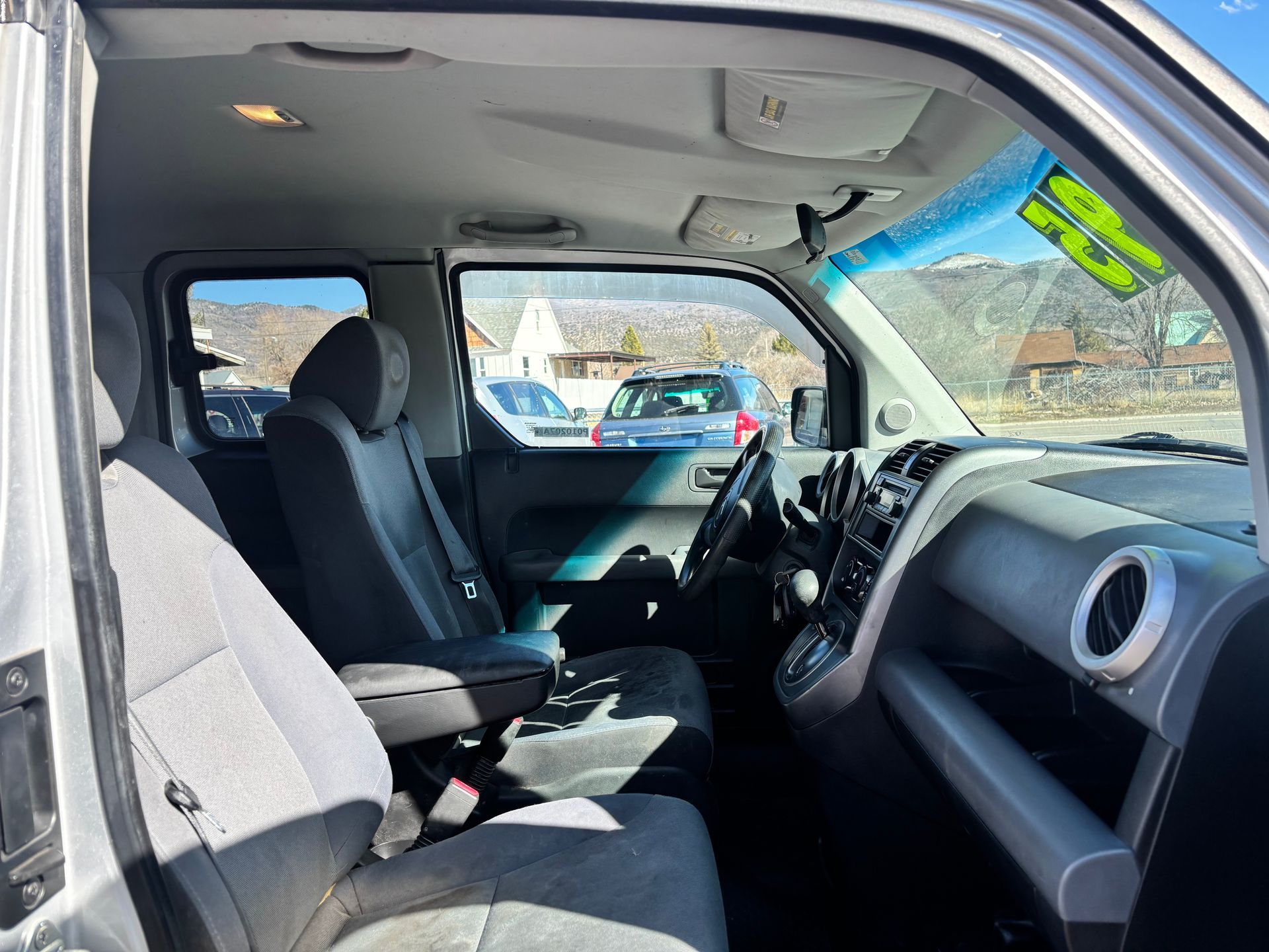 Interior of a parked vehicle with black seats, dashboard, and rearview mirror visible through the open side door.