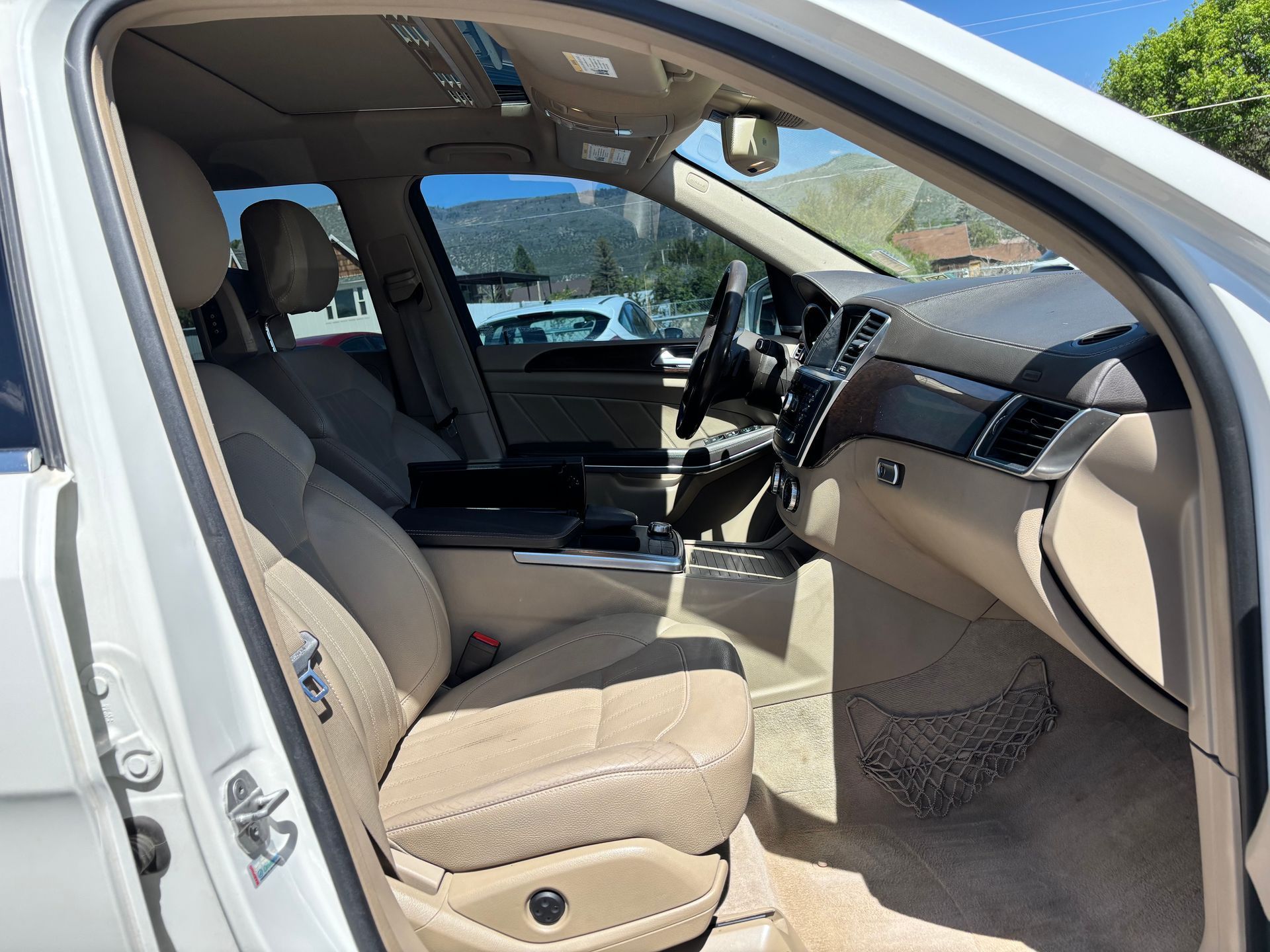 Open car door showing beige front seats and dashboard inside a white vehicle.