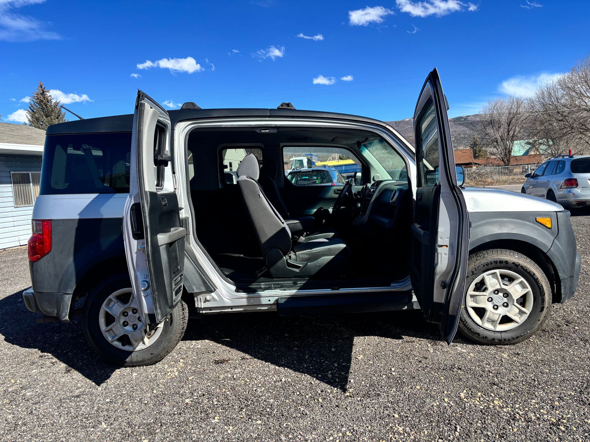 Silver SUV with both right-side doors open, parked on gravel in bright sunlight.