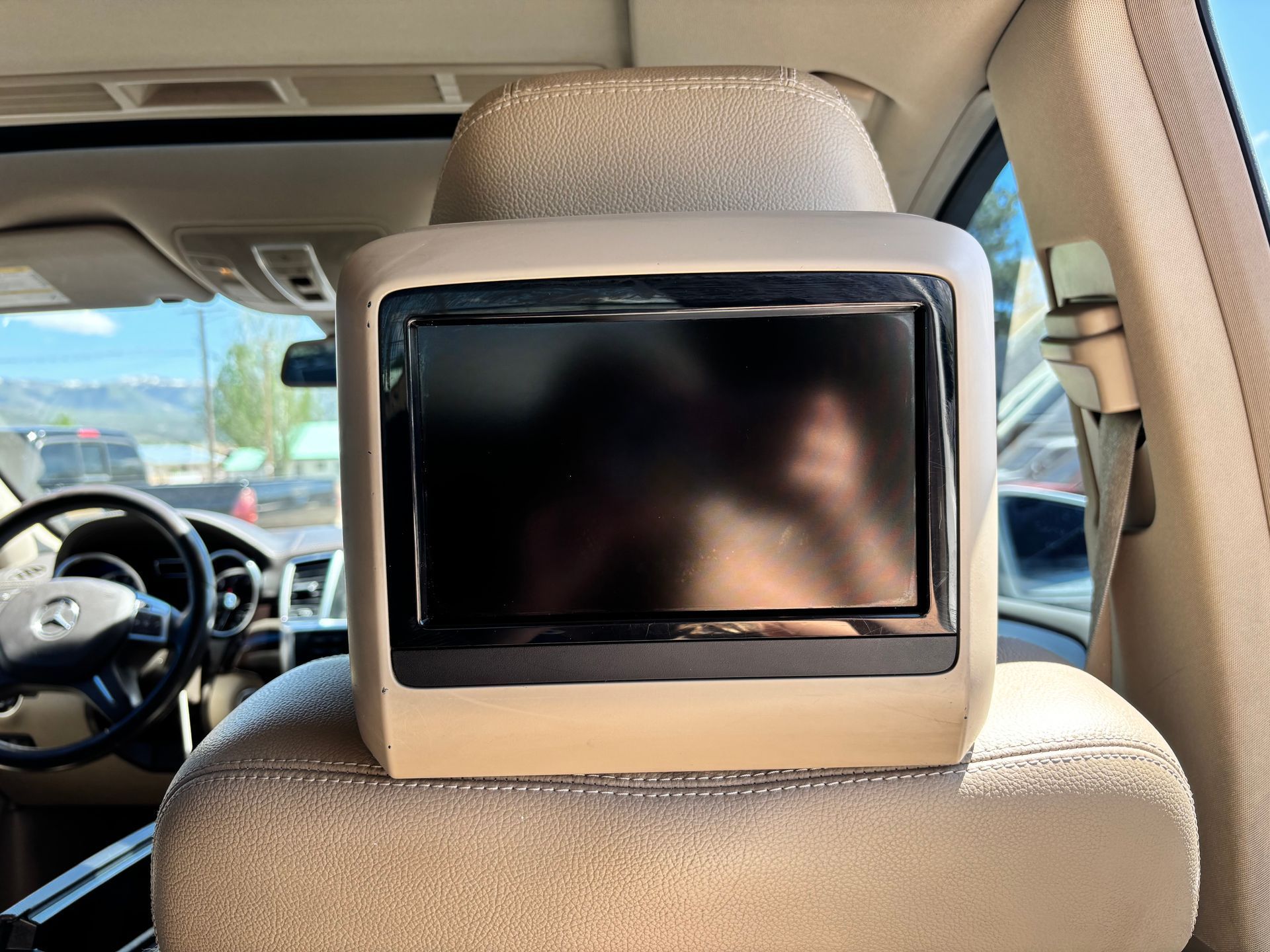 Rear-seat entertainment screen mounted on a beige car headrest inside a vehicle