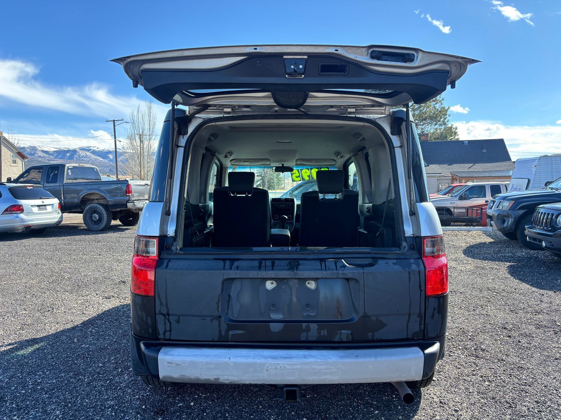 Open rear cargo van with hatch raised in a gravel parking lot under a blue sky