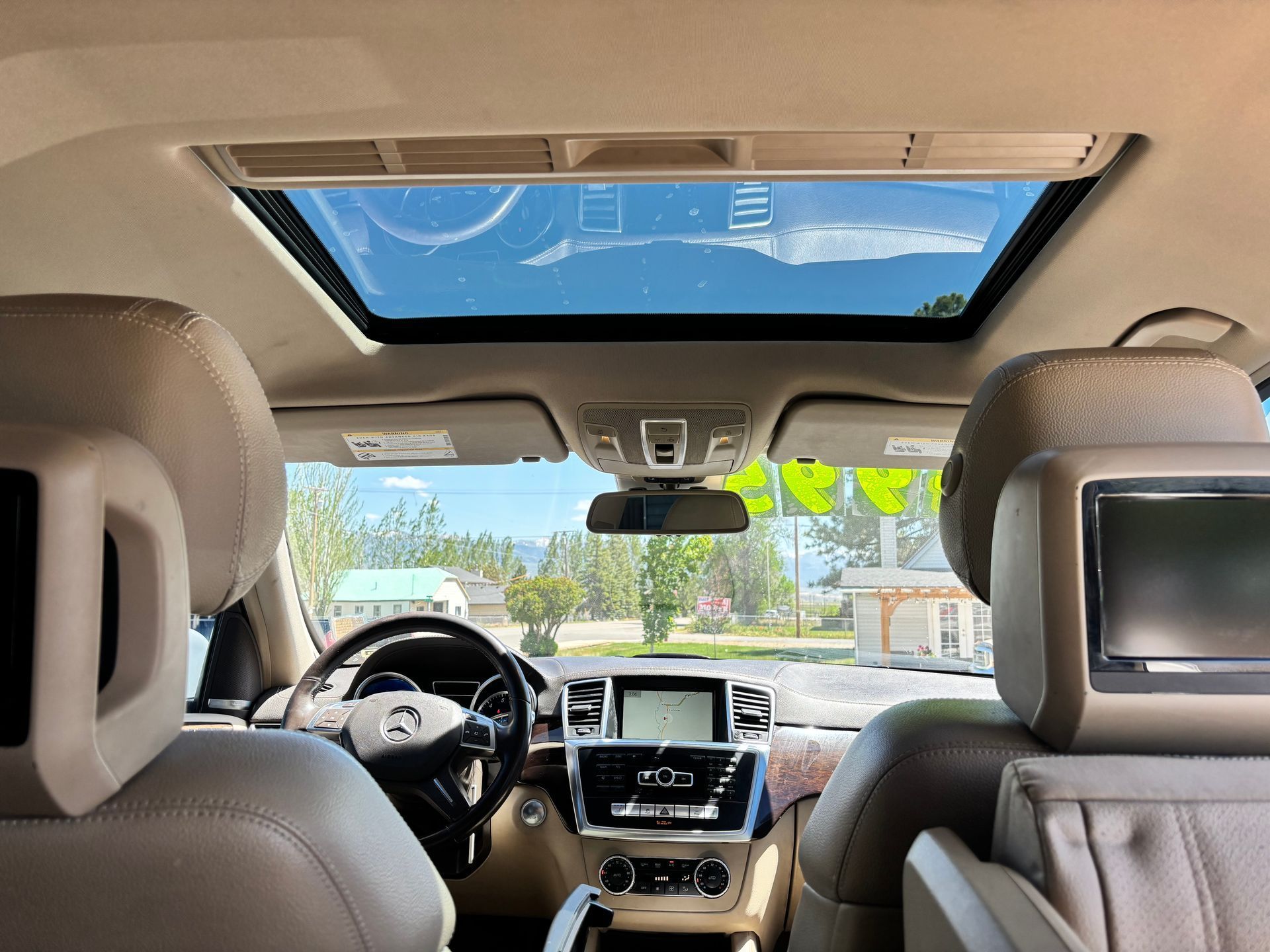 Inside a car, beige interior with sunroof and dashboard, looking out at a bright street scene.