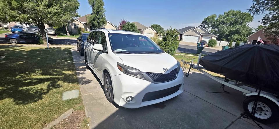 White sedan parked in a suburban driveway beside a covered trailer on a sunny day