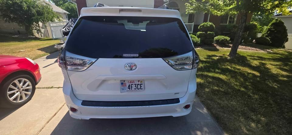 White Toyota SUV parked in a driveway, viewed from the rear, with a red car beside it.