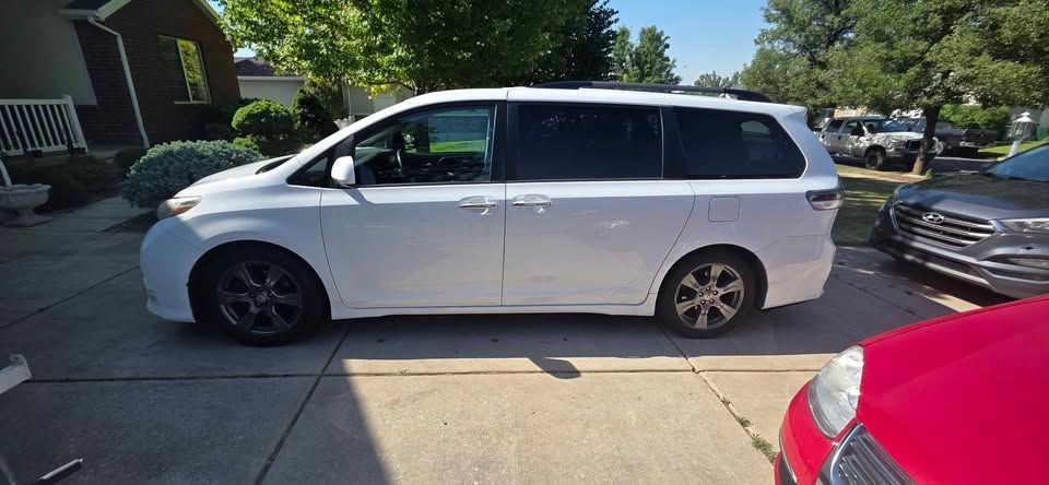 White minivan parked in a driveway beside a red car on a sunny residential street