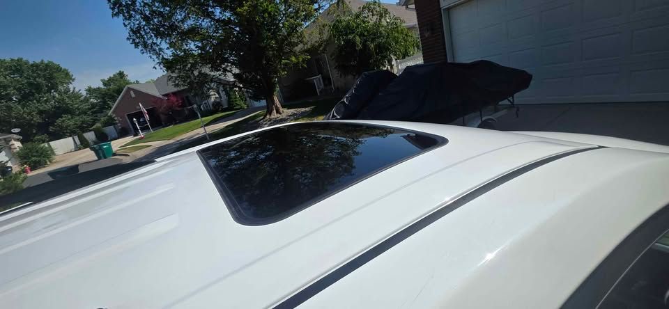 White car roof with an open sunroof on a sunny suburban street