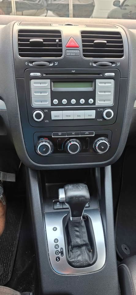 Car dashboard center console with stereo, climate controls, hazard button, and automatic gear shifter.