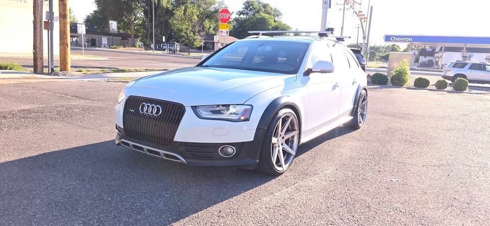 Silver Audi sports car parked on a sunny street corner near a stop sign and buildings