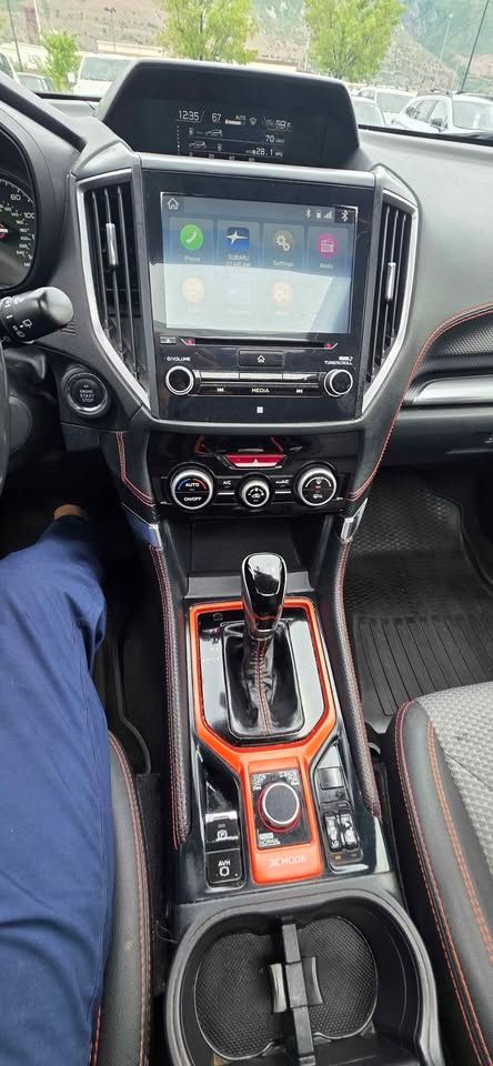 Car interior with center console, touchscreen, gear shift, and cup holder in black and orange trim.