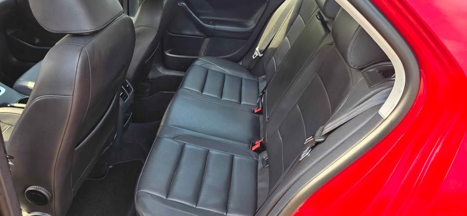 Red car interior showing black leather back seats and front seat backs, viewed through the open rear door