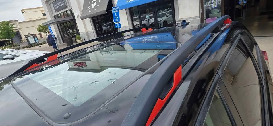 Roof rack and red trim on a parked car outside storefronts, viewed from above