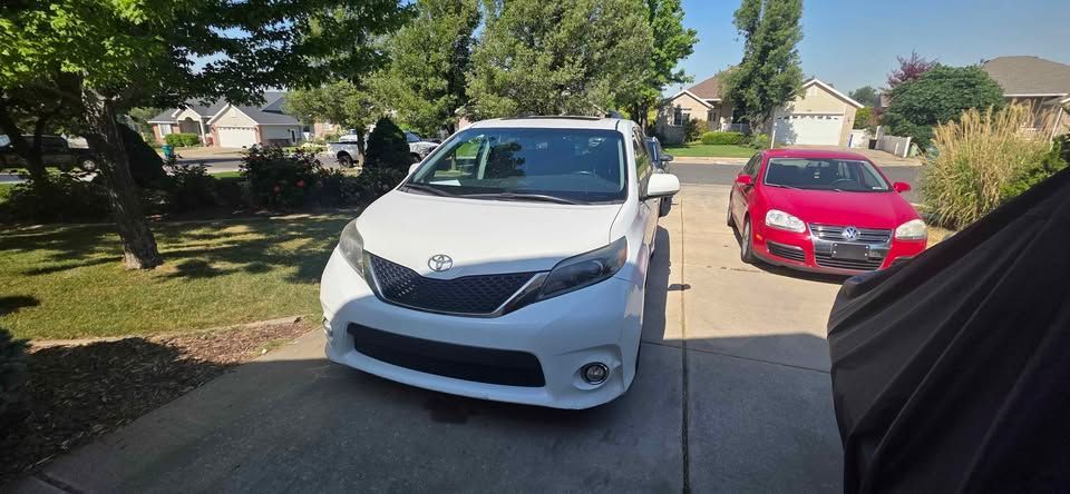 White sedan in a driveway with a red car parked on the right and houses in the background.