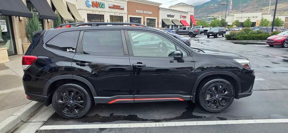Black SUV parked on a street in front of storefronts, with red trim along the lower side.