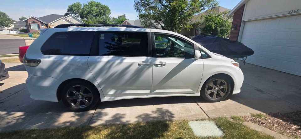 White minivan parked in a driveway beside a garage on a sunny suburban street