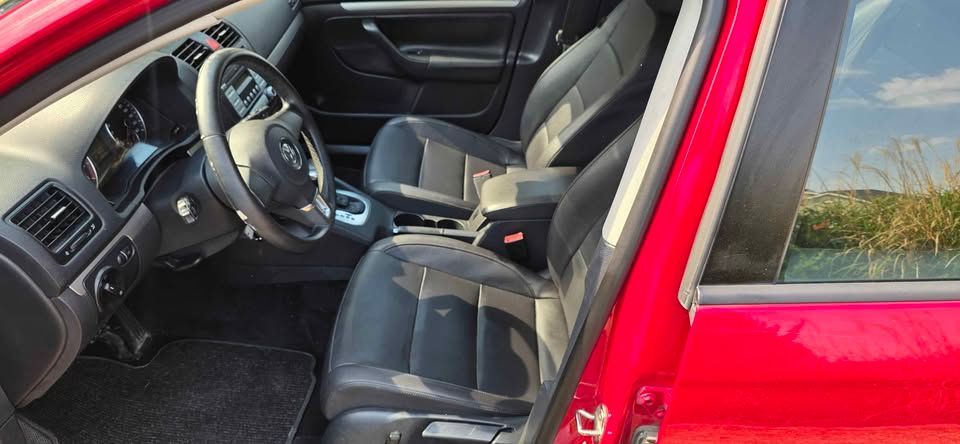 Red car interior with open door, showing the driver’s seat, steering wheel, and dashboard.