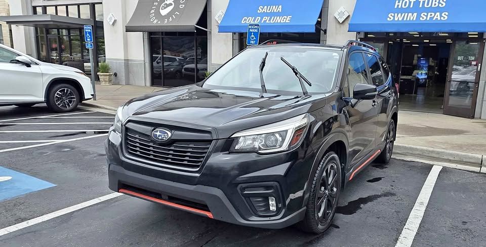 Black Subaru SUV parked in a storefront lot on a rainy street, with a red trim on the front bumper