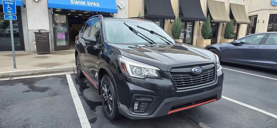 Black Subaru SUV parked on a street in front of shops, with red trim on the front bumper.