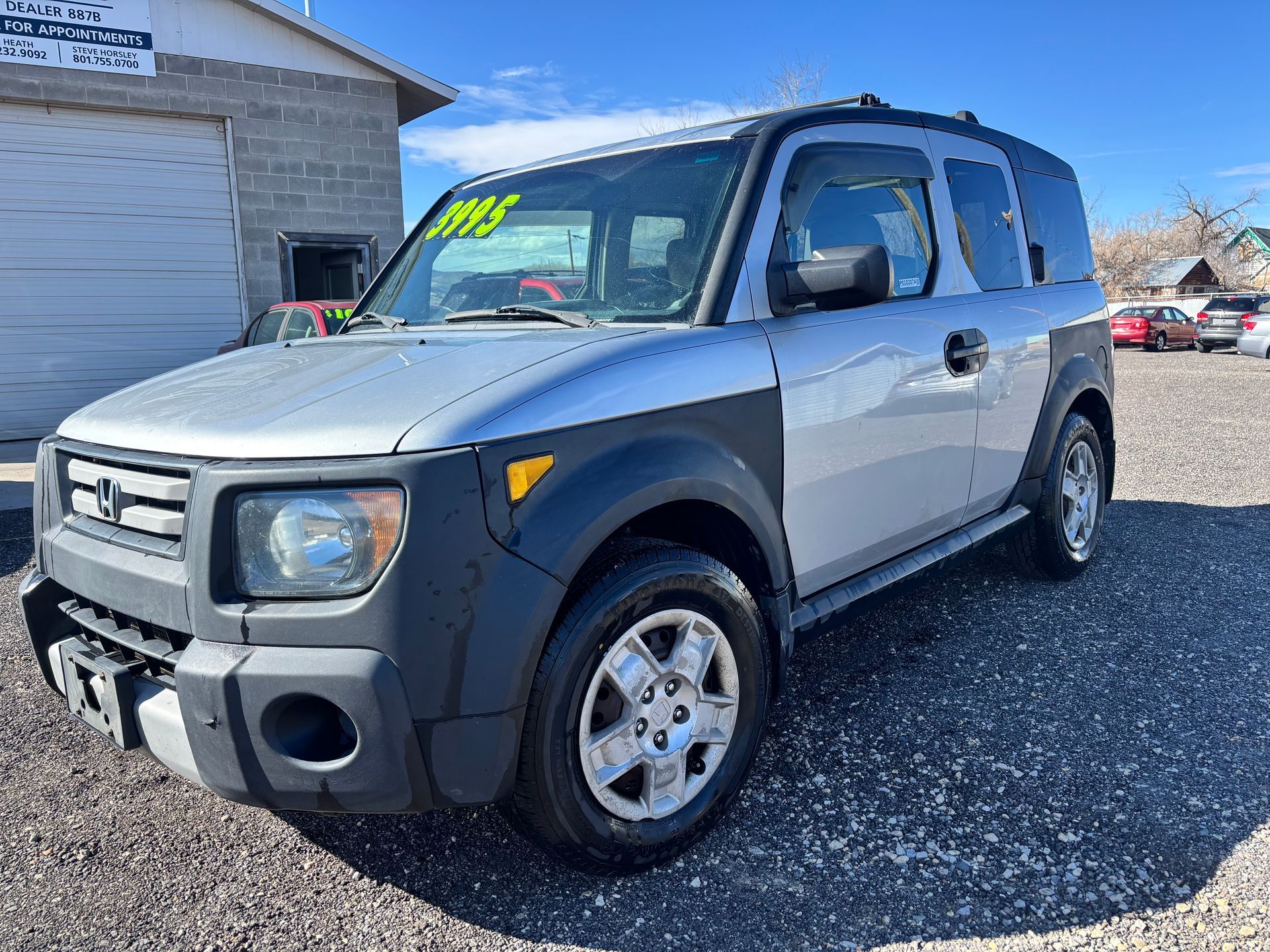 Silver Honda Element parked on gravel beside a building on a sunny day