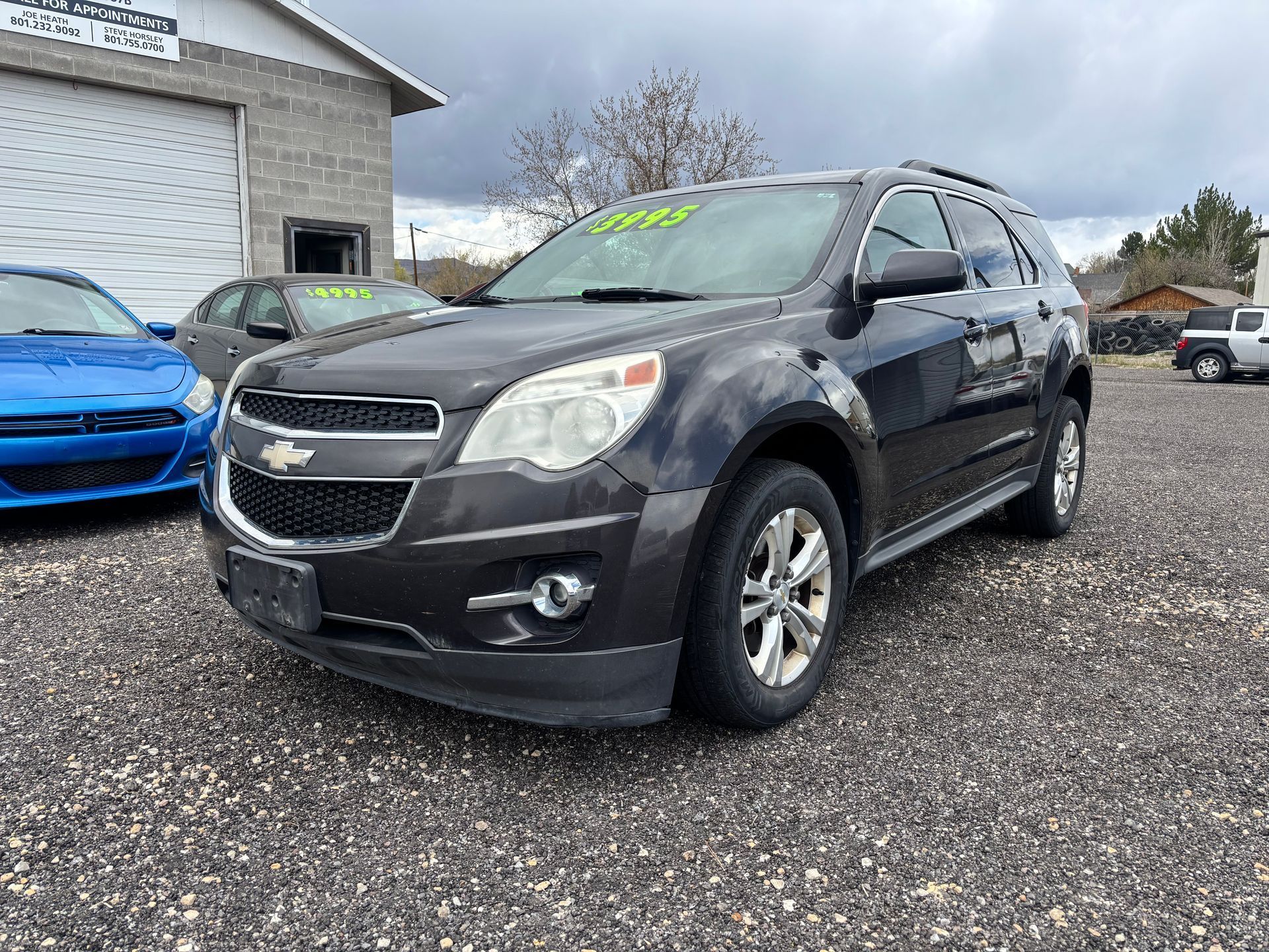 Black Chevrolet SUV parked on a gravel lot beside a house, with a blue car in the background.