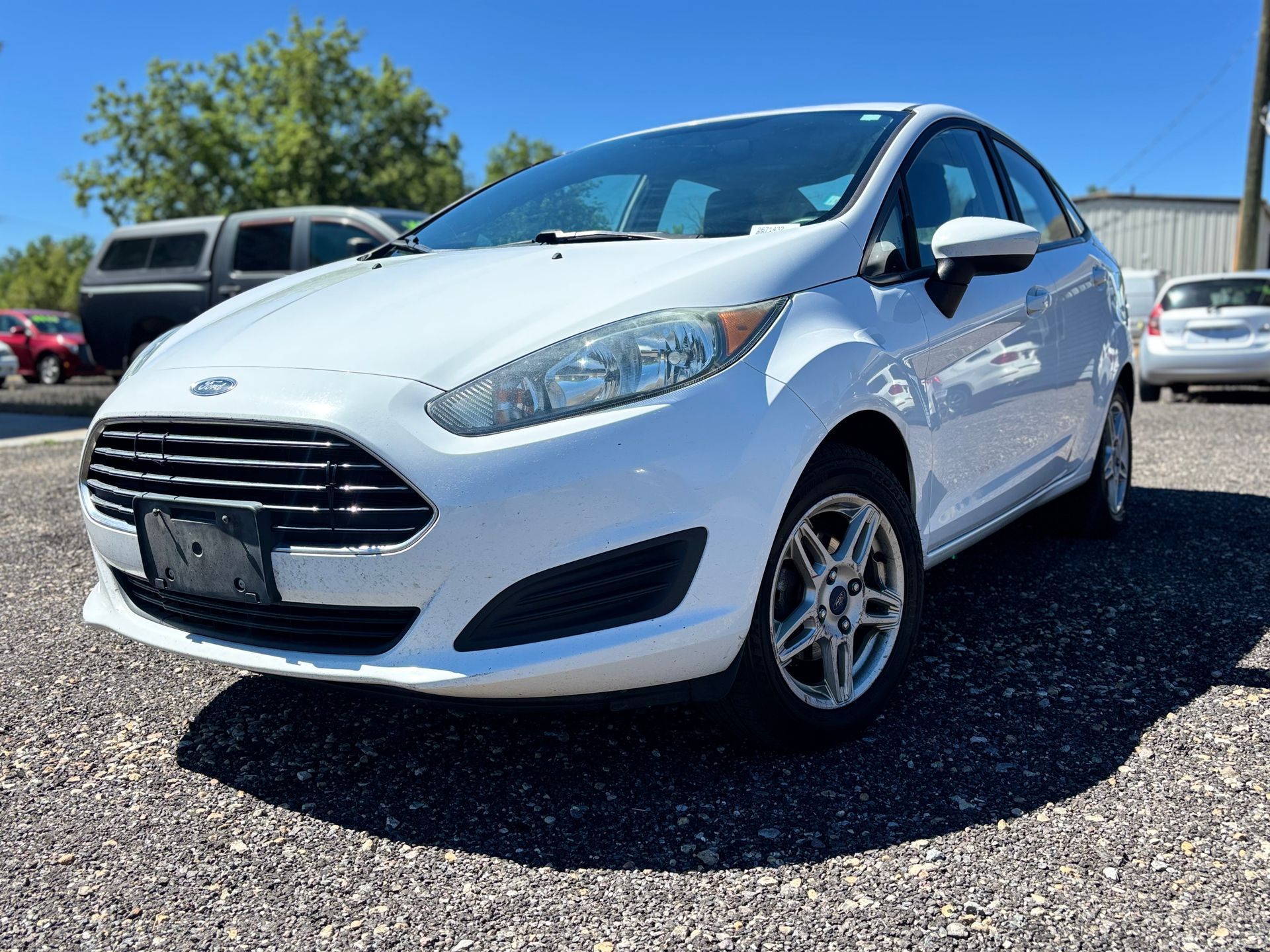 White Ford hatchback parked on a gravel lot under a clear blue sky