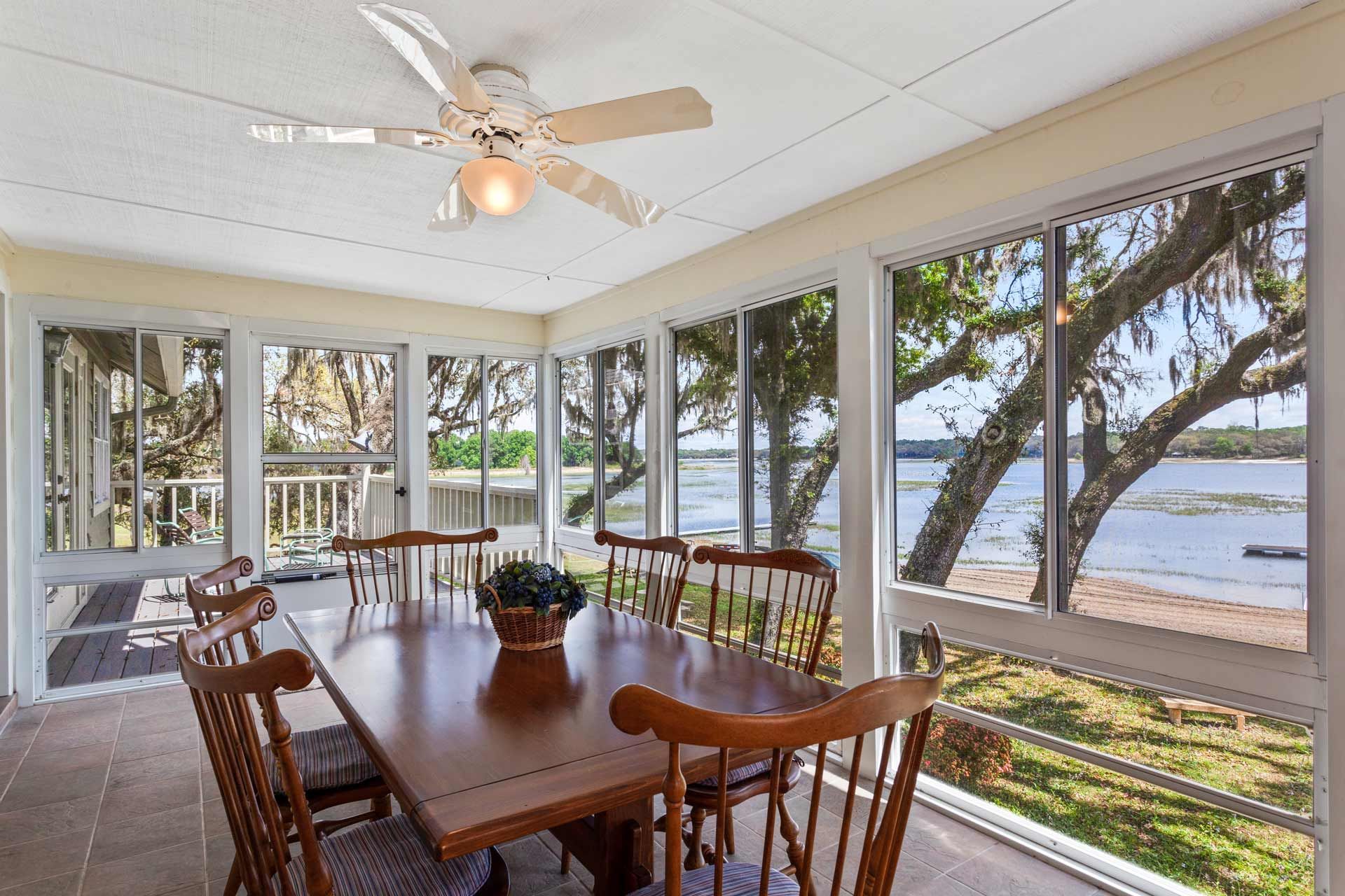 Sunroom with table and chairs, overlooking water and trees.