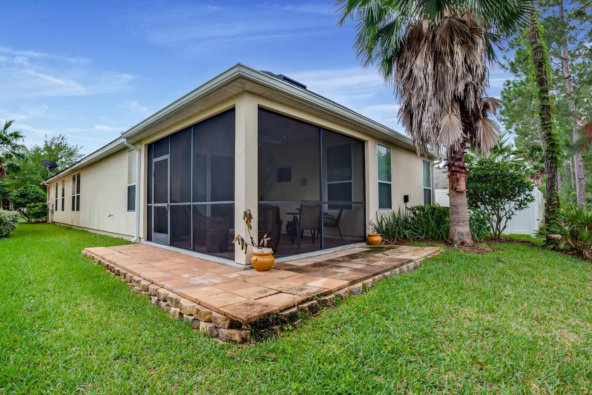 Backyard with a screened porch, surrounded by green grass and a palm tree.