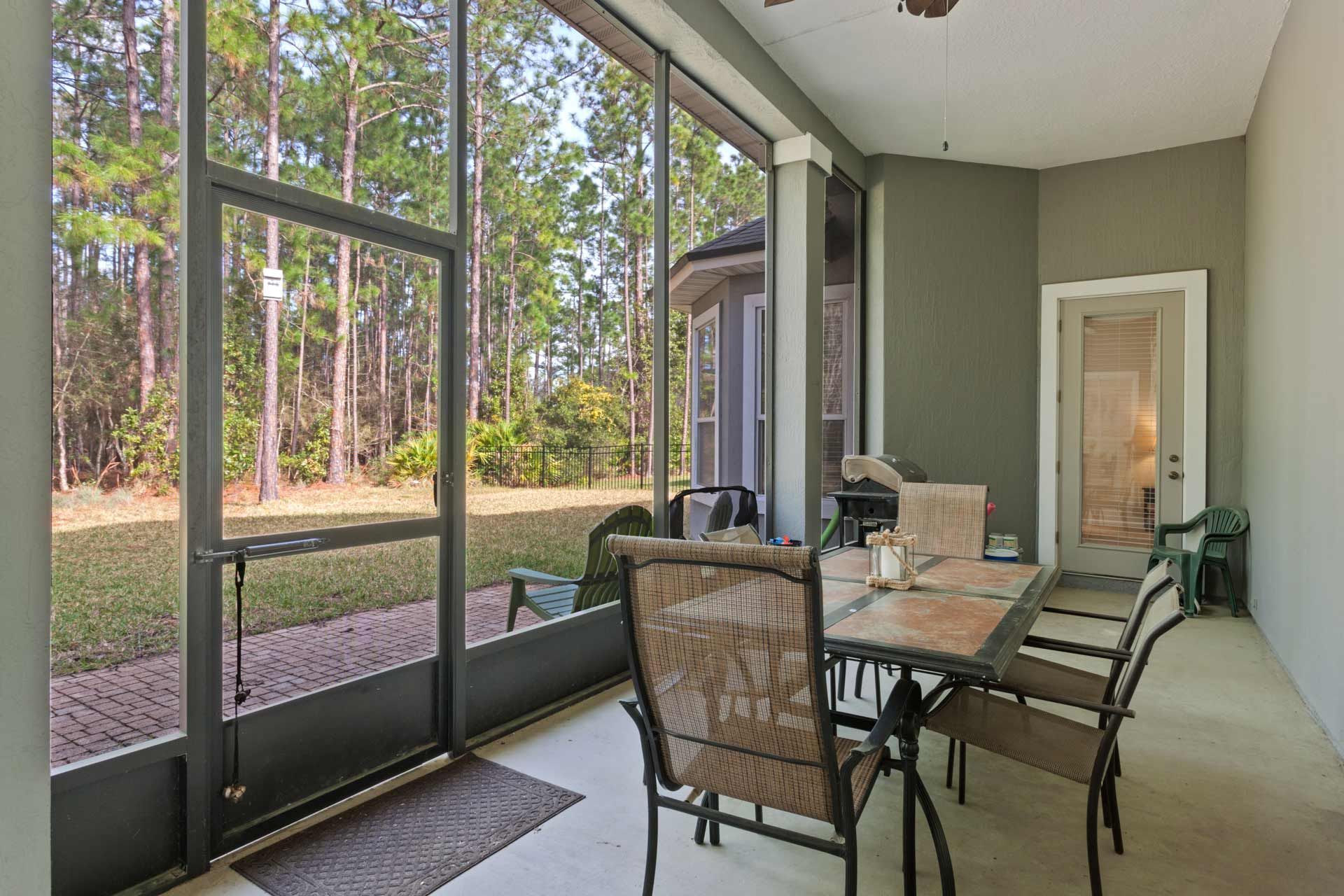 Screened-in patio with dining table, chairs, and view of a wooded backyard.