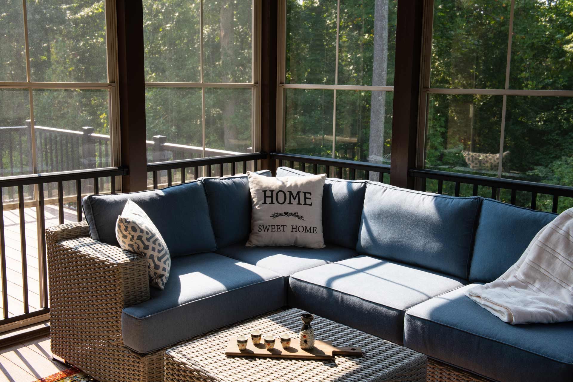 Cozy screened porch with blue sectional, neutral woven coffee table, and 