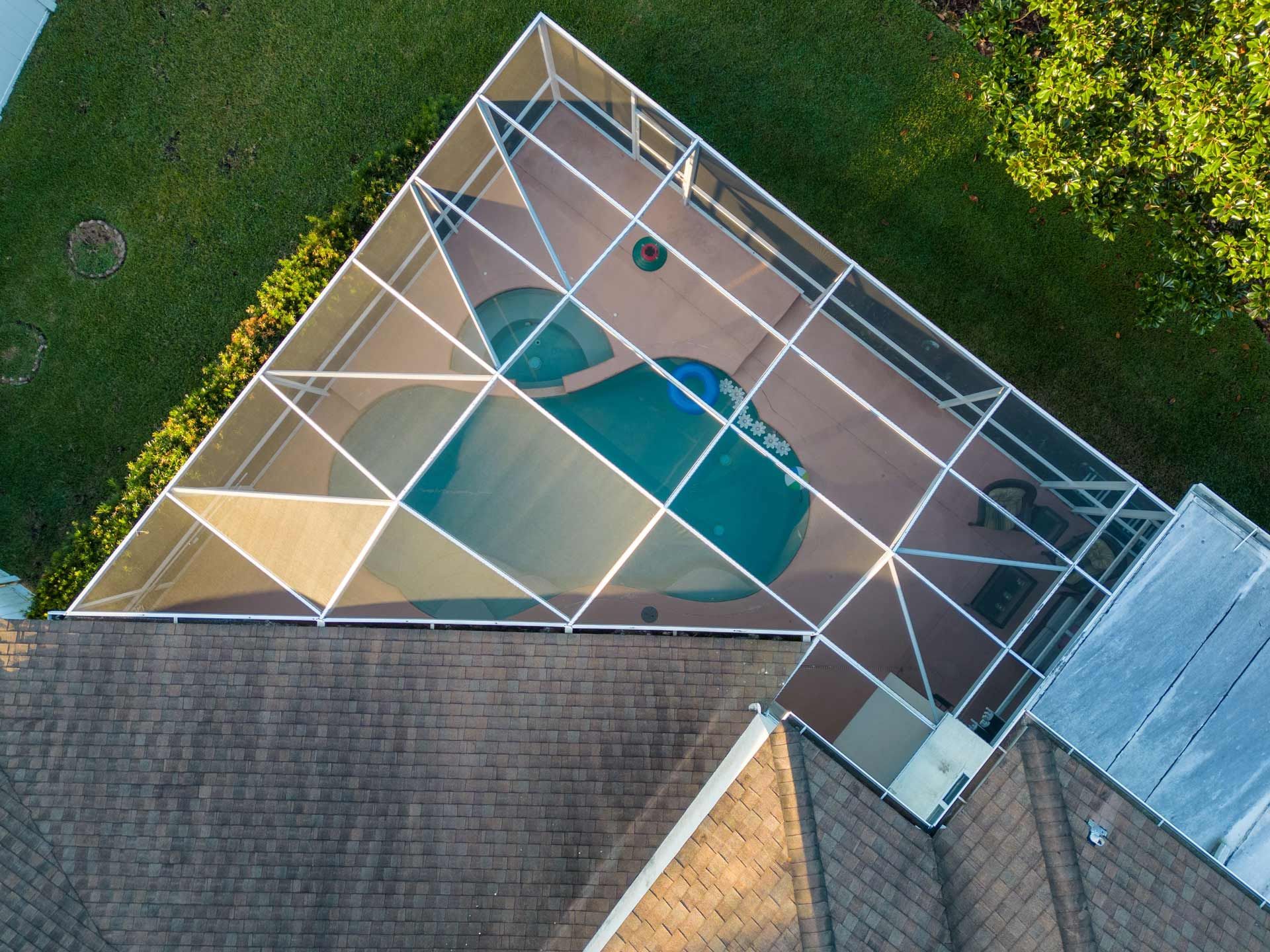 Aerial view of a pool enclosed in a screened structure, next to a house.
