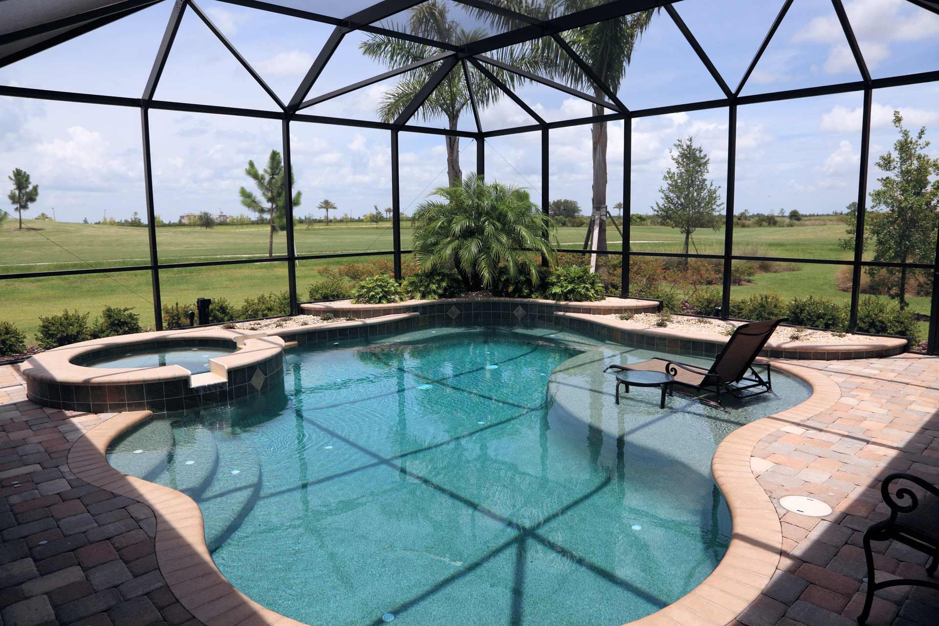 A pool and hot tub enclosed in a screen enclosure with outdoor landscaping.