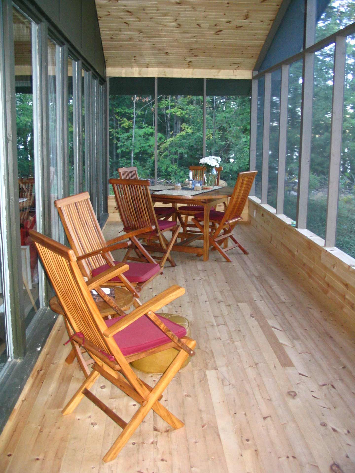 Screened porch with wood floor and folding chairs; table set for dining overlooking trees.