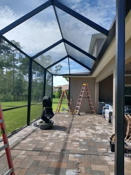 Screened-in patio extension with black frame, brick pavers, ladders.