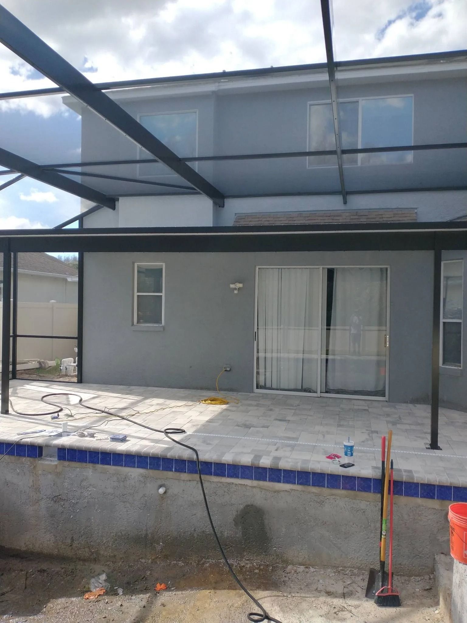 Backyard with a pool, patio, and gray house under construction.