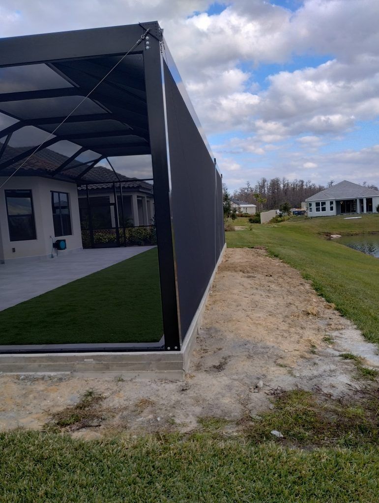 Outdoor patio with black screen enclosure, artificial grass, and a water feature.