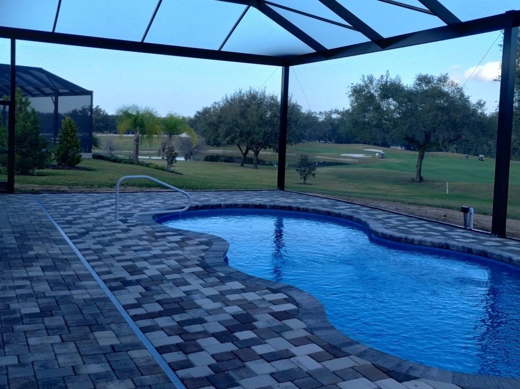 Pool under a dark-framed patio. The pool is blue, surrounded by brick pavers.