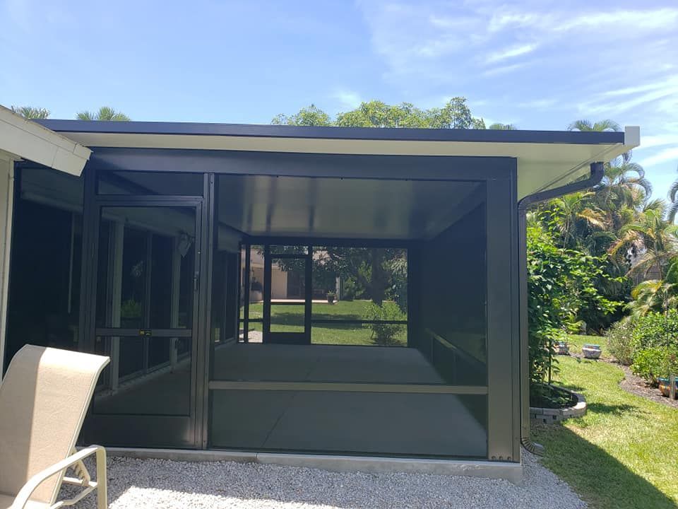 Screened-in patio with dining table, chairs, and view of a wooded backyard.