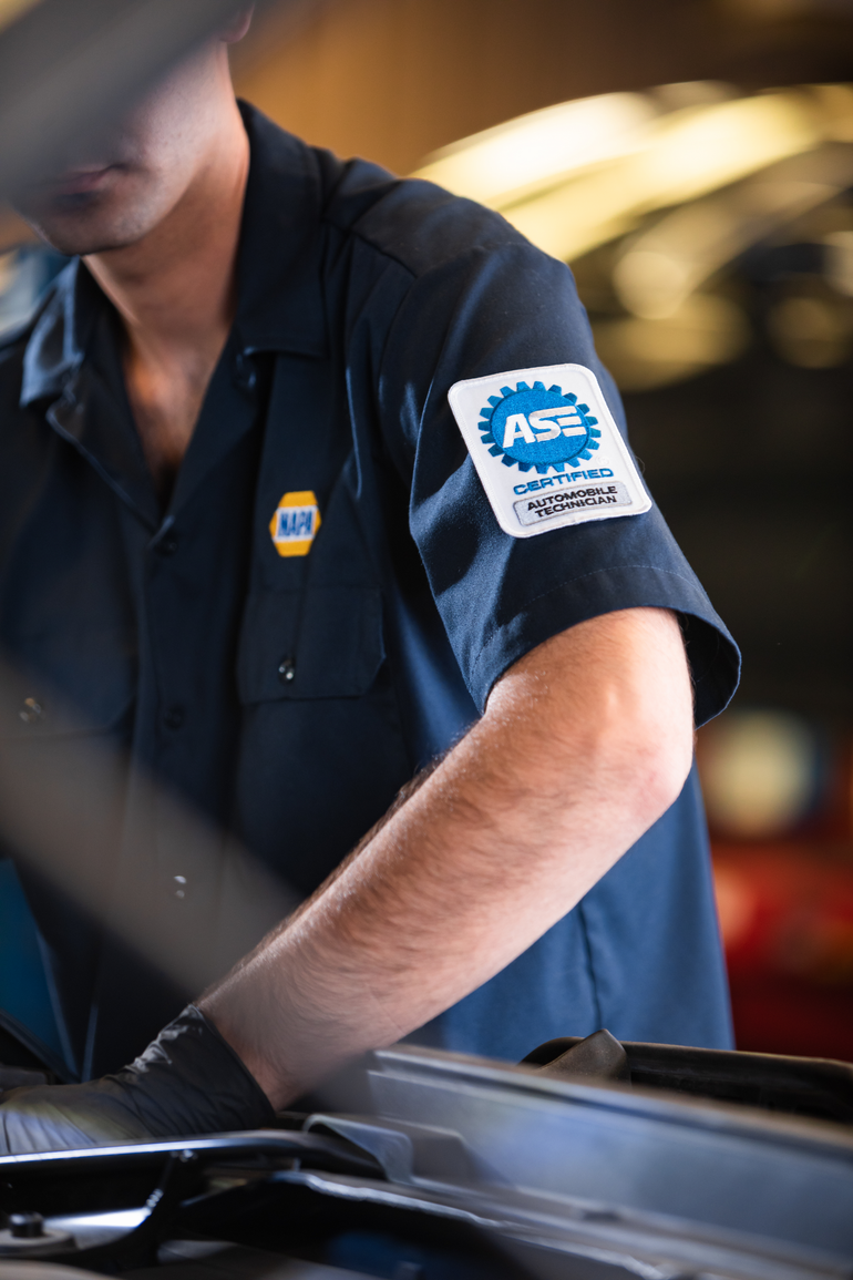 Mechanic in a dark blue uniform working on a vehicle engine in a shop.