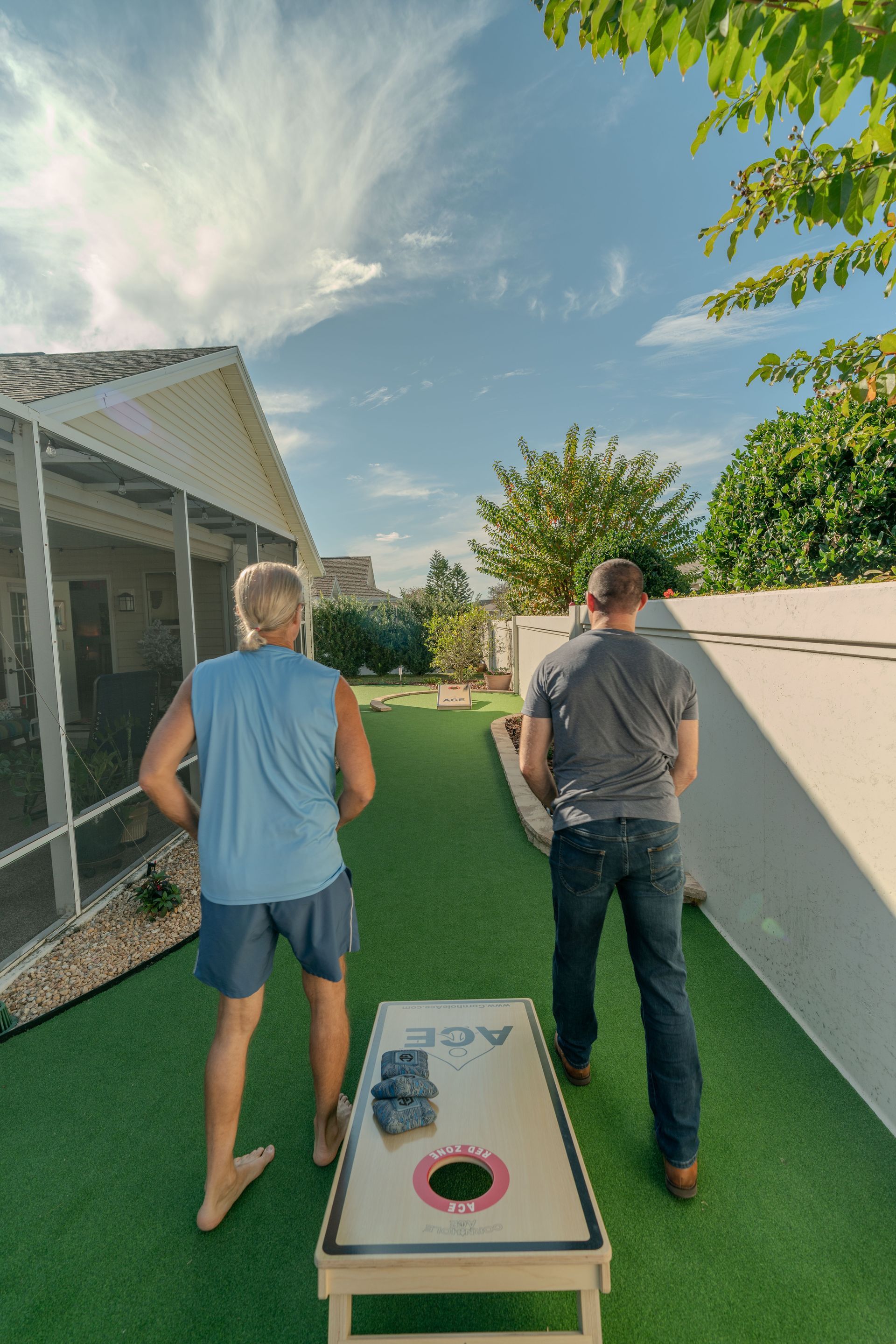 Two people playing cornhole on a green lawn; sunny day, blue sky.