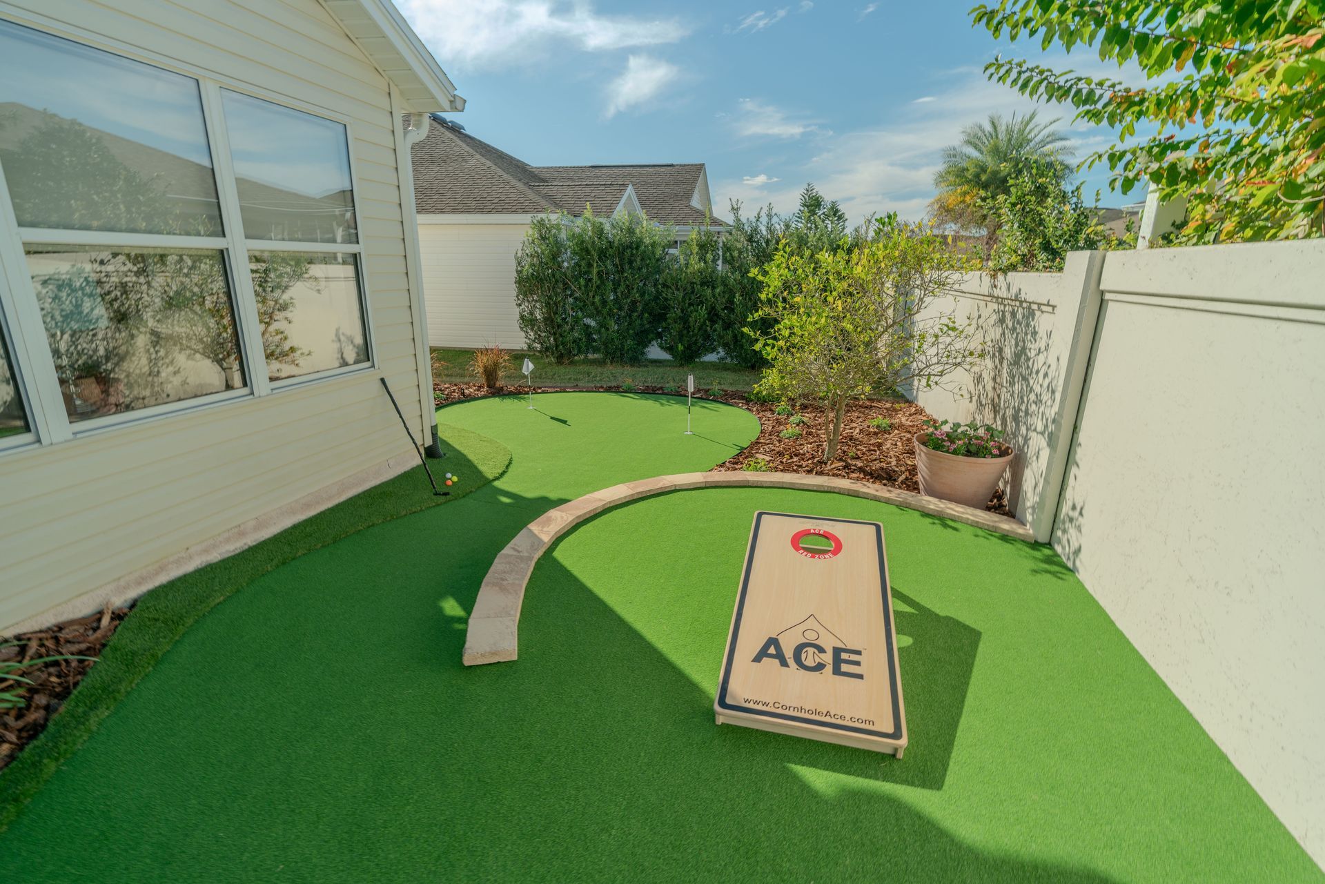 Backyard with artificial turf, mini-golf course, and cornhole game. Green, white, and brown colors.