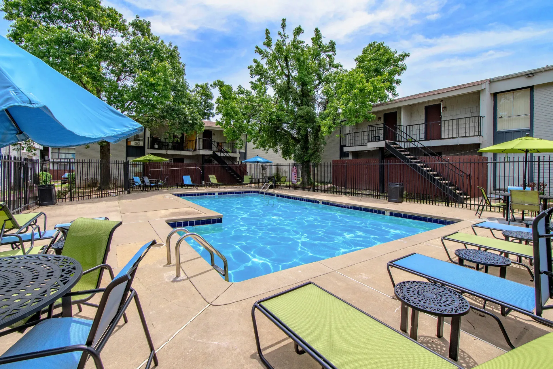 Outdoor apartment pool area with lounge chairs, tables, and umbrellas.