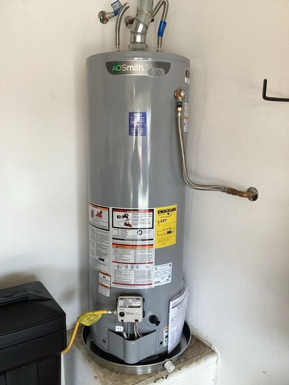 A grey A.O. Smith gas water heater sits in a drain pan on a raised platform in a garage.