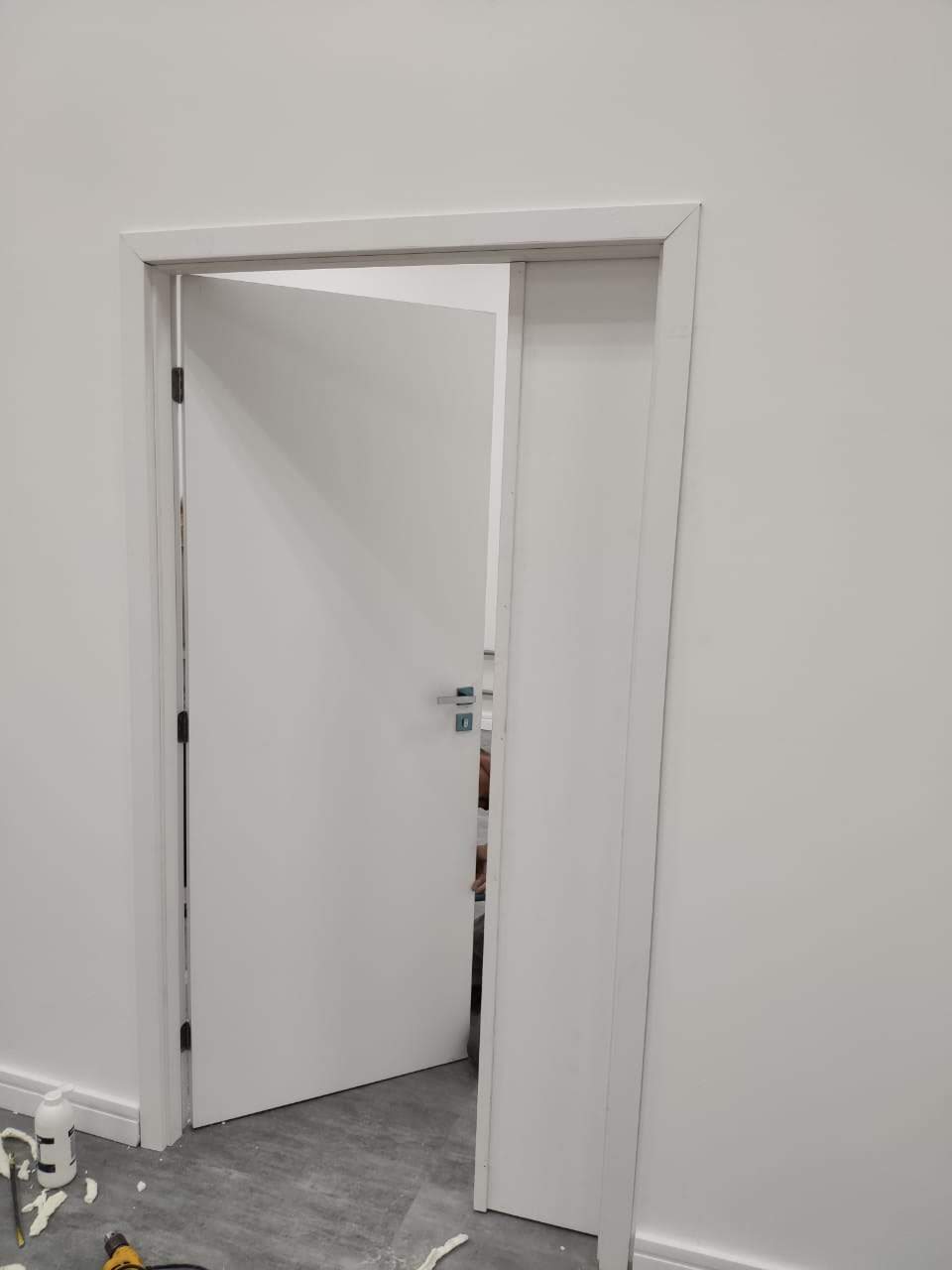 Uma porta branca está aberta em uma sala com uma parede branca.