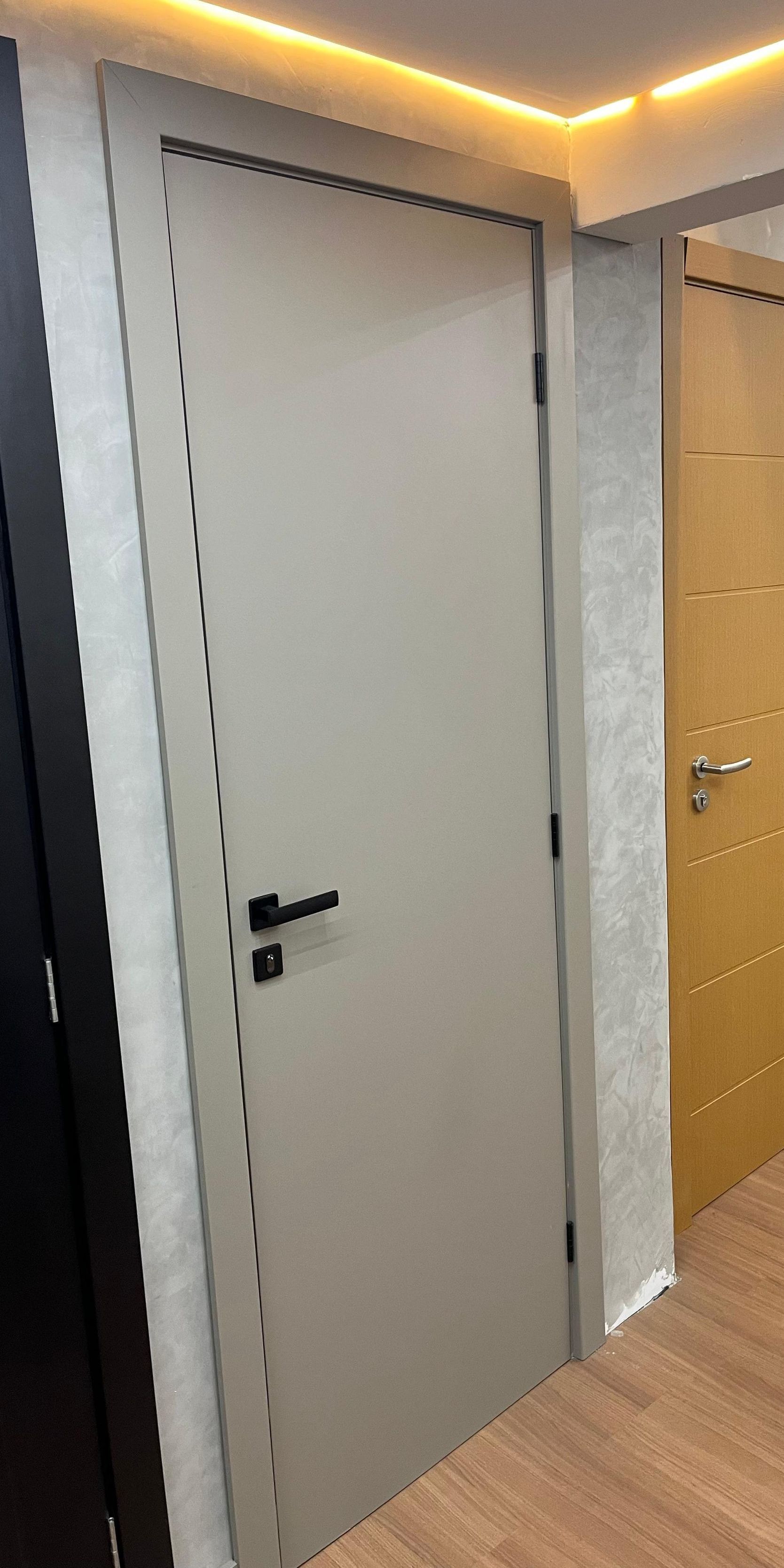 Uma porta branca com uma maçaneta preta está em um corredor.
