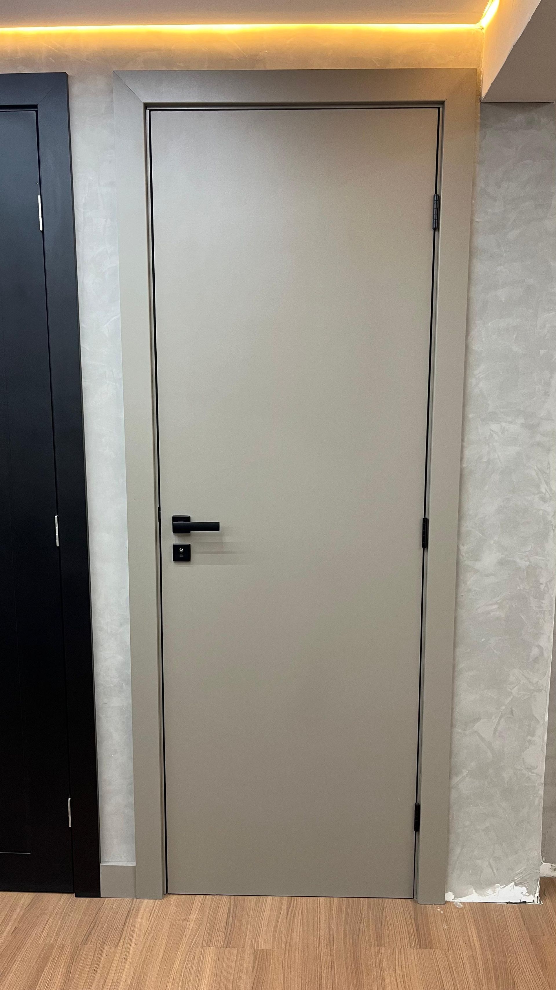 Uma porta branca com uma maçaneta preta está em uma sala ao lado de uma porta preta.