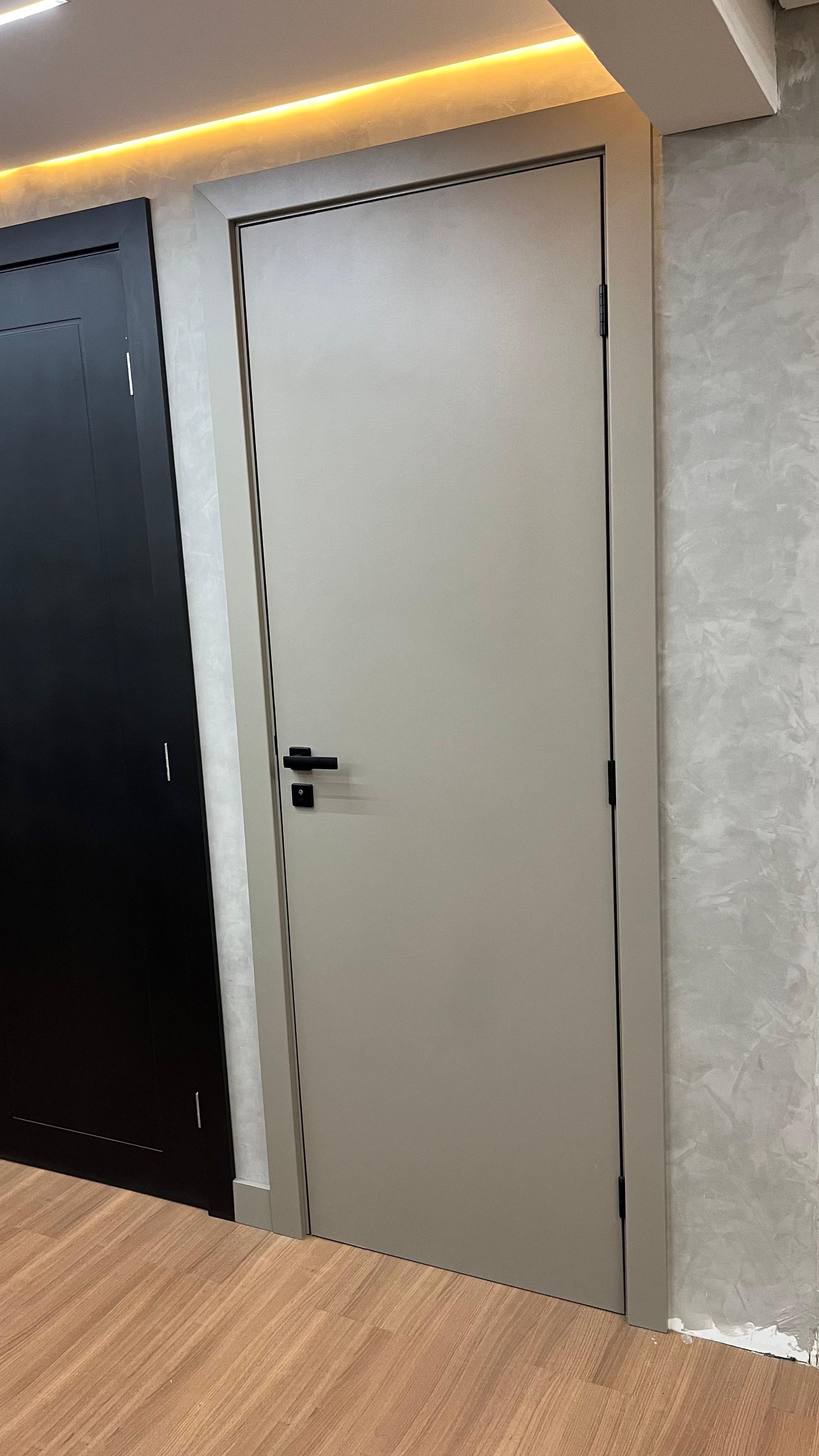 Uma porta branca com uma maçaneta preta está em uma sala ao lado de uma porta preta.