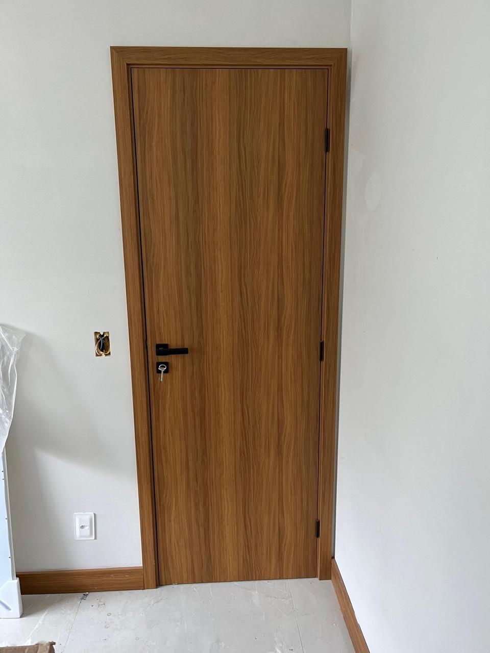 Uma porta de madeira está em uma sala ao lado de uma parede branca.