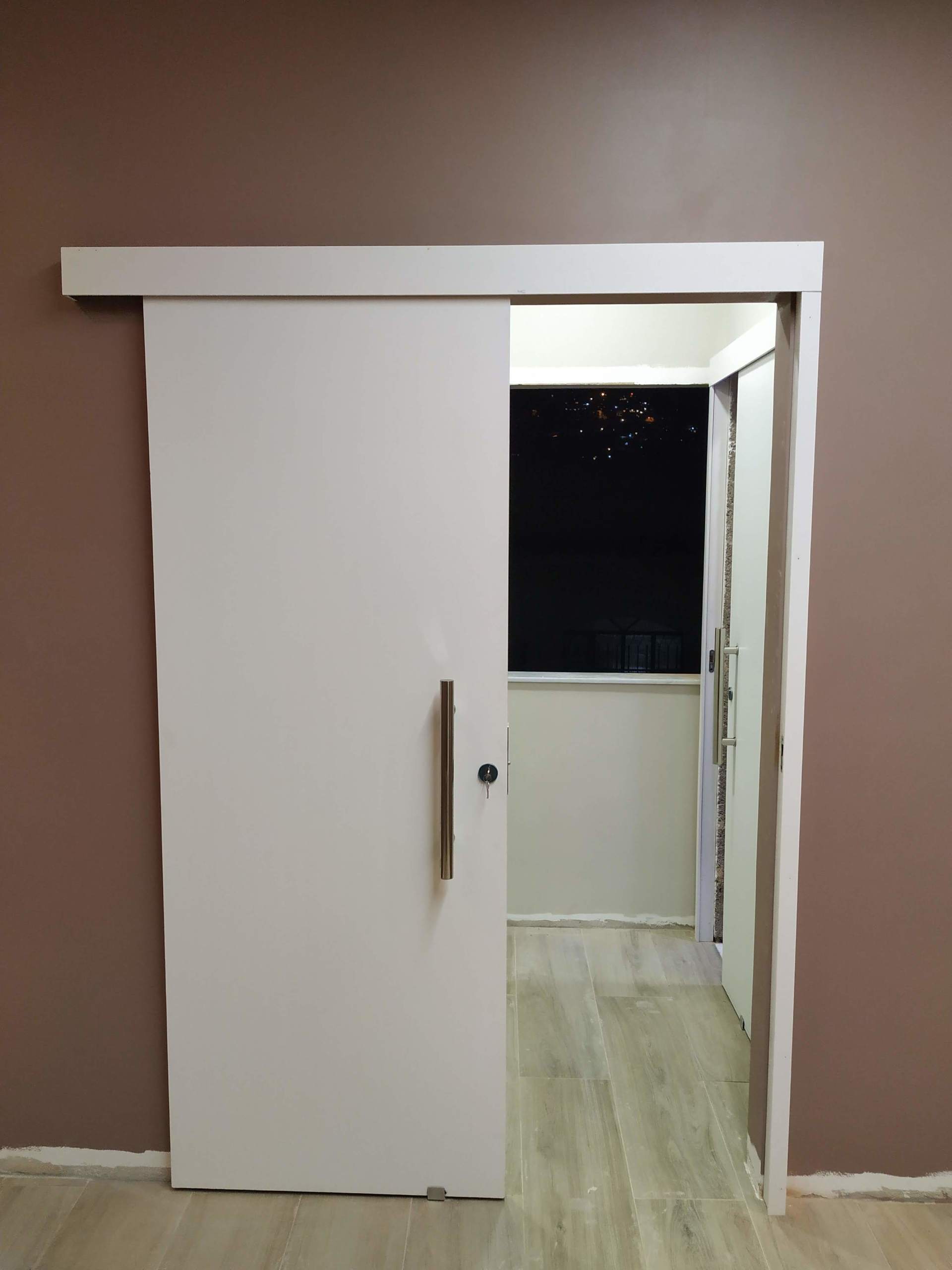 Uma porta de correr branca está aberta para uma sala com paredes marrons.