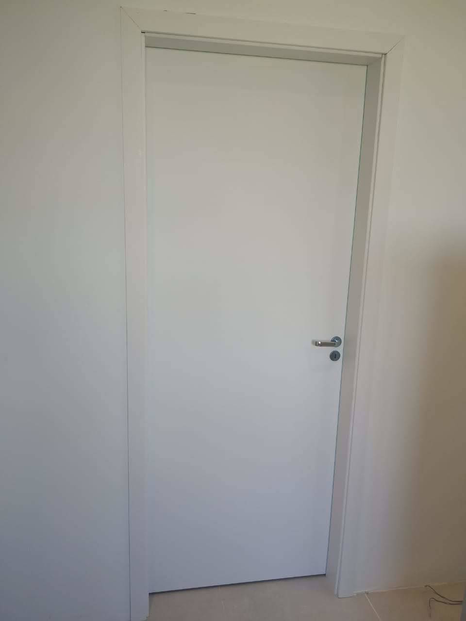 Uma porta branca está em uma sala ao lado de uma parede branca.