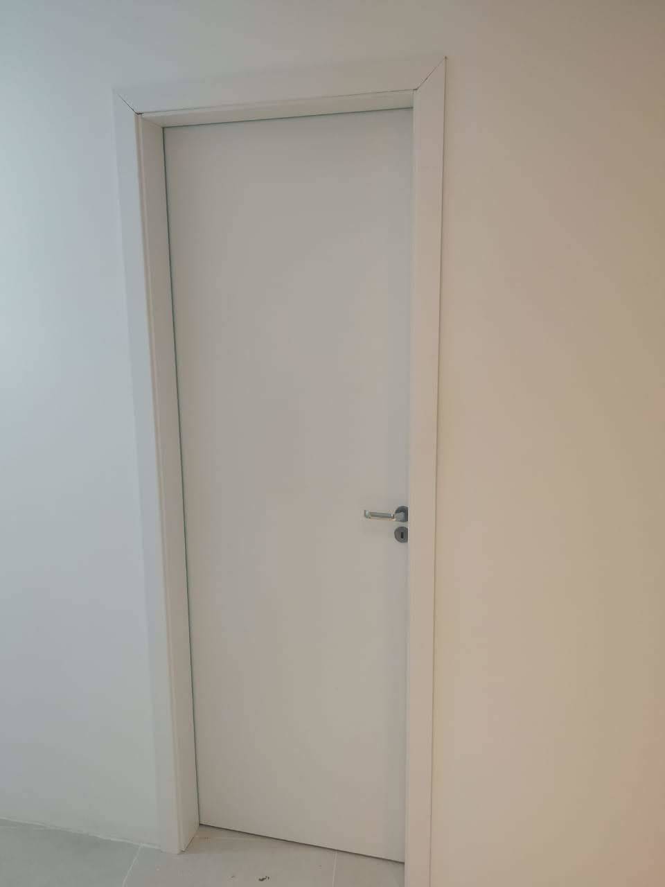 Uma porta branca está em uma sala ao lado de uma parede branca.